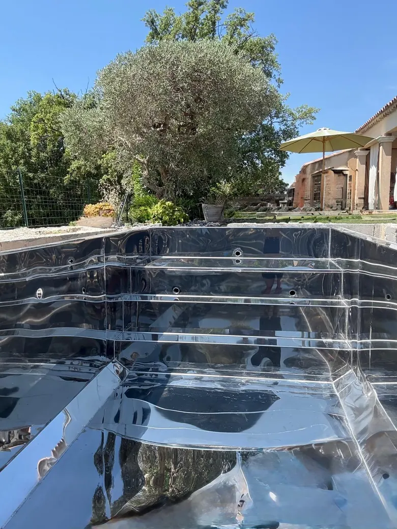 Cuve de piscine en inox poli posée dans sa fouille, escalier intégré, avant mise en eau.