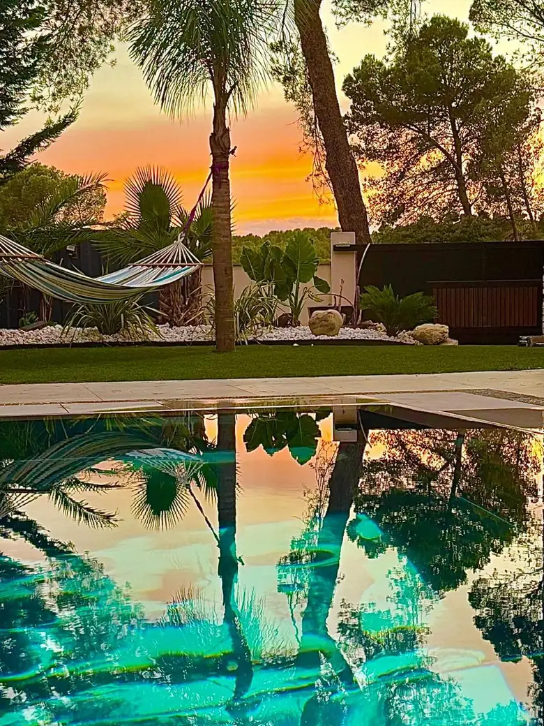Bassin au crépuscule, palmiers et hamac dans le jardin.